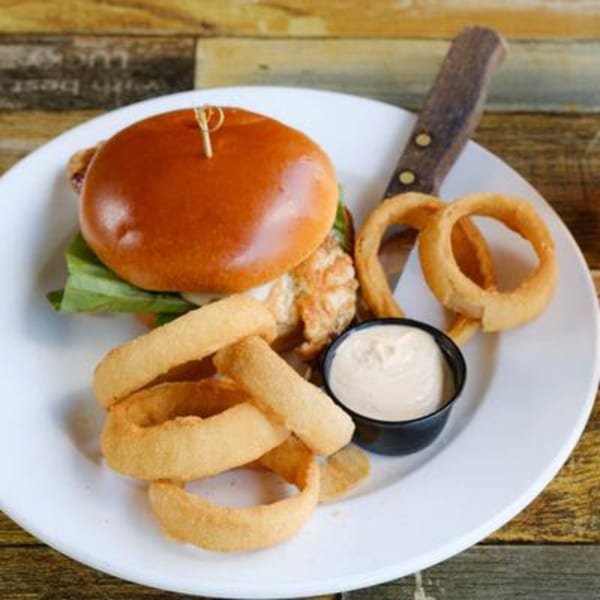 A Rusty Onion burger with lettuce, onion rings, and a side of dipping sauce on a white plate.