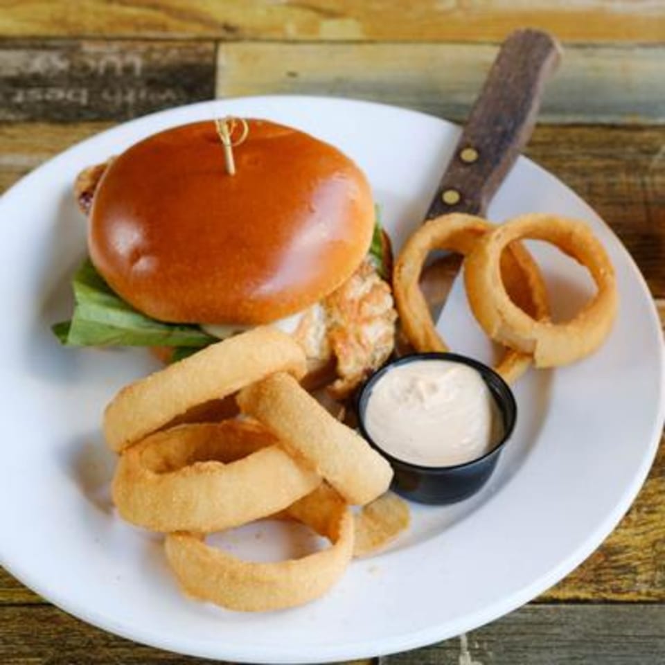 A Rusty Onion burger with lettuce, onion rings, and a side of dipping sauce on a white plate.