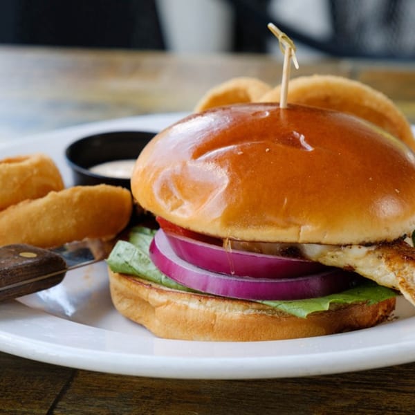 Chicken sandwich with red onion, lettuce, and a side of onion rings and dipping sauce.