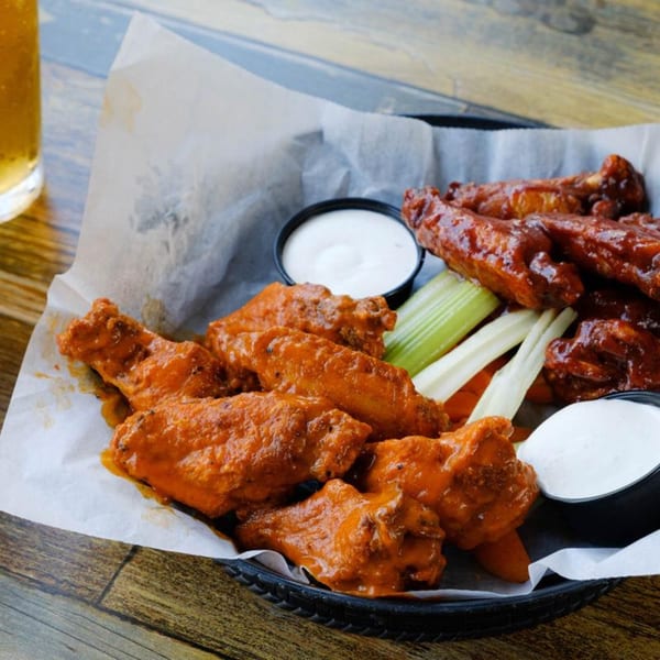 A basket of The Rusty Onion's buffalo wings with celery, carrots, and two dipping sauces.
